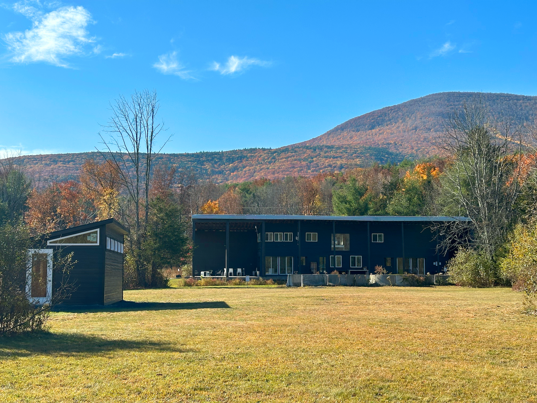 photograph of the Outer Space listening gallery in the foreground. The Wave Farm Study Center building in the background, against the Catskill Mount Park in peak fall foliage